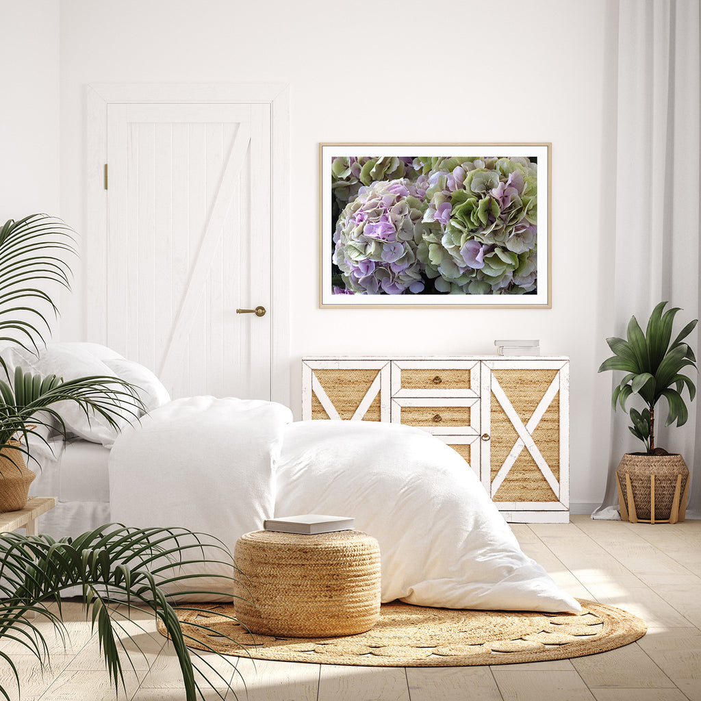 Bedroom with white bedding, raffia ottoman, and framed flower picture on wall