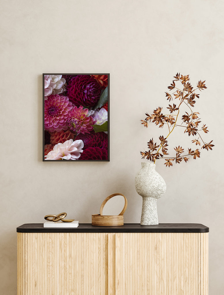 Decorative setup with a floral painting, vase, and mirror on a wooden cabinet against a beige wall.